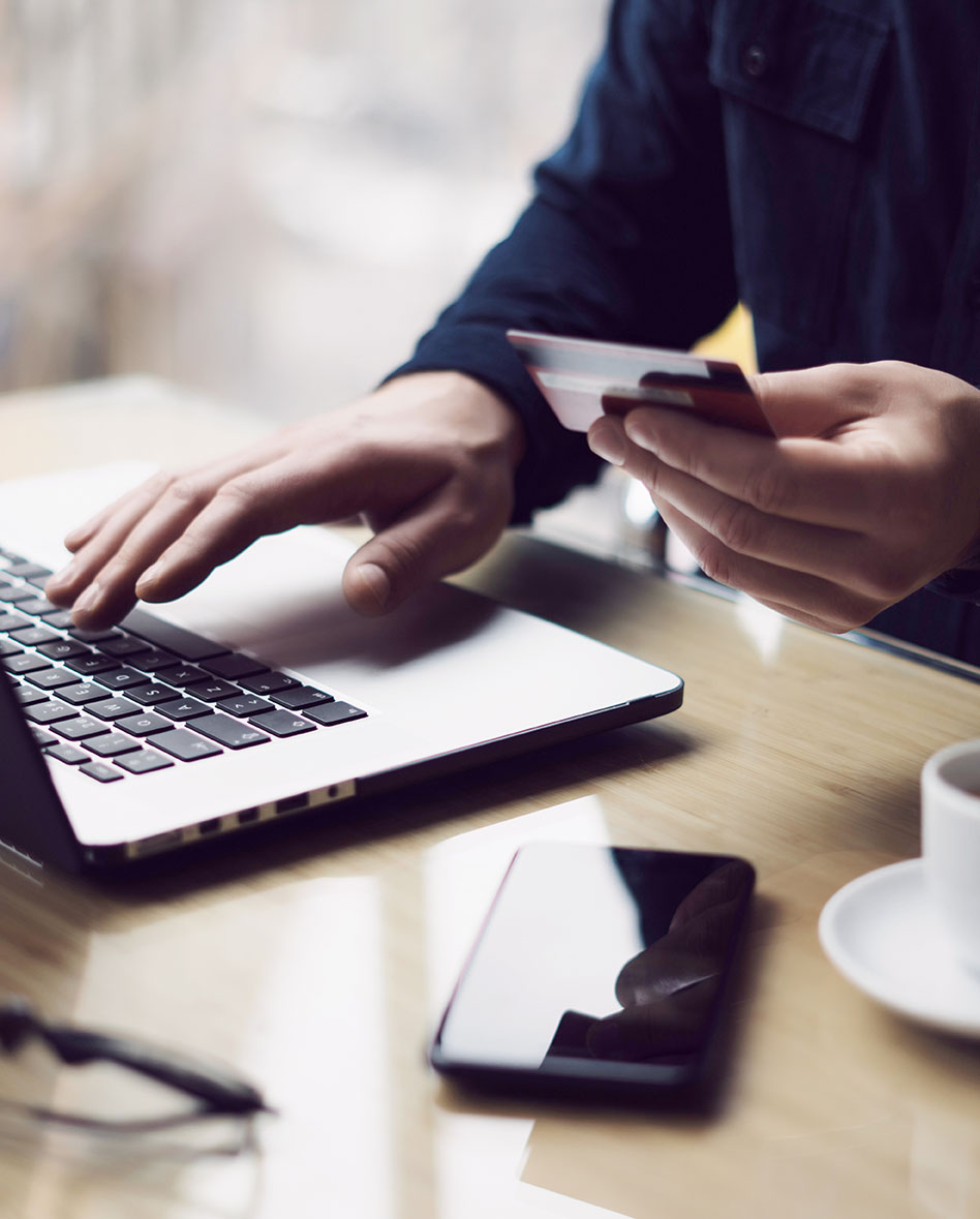 Businessman holding plastic credit card in hand and using laptop computer while sitting at the wooden table.Man making online shopping.Blurred background.Vertical.